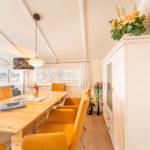 Dining area with wooden table, orange chairs, and windows overlooking the landscape.