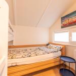 Room with double bed, radiator, and windows with blinds.