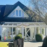 Haus mit Glasveranda und Dachfenster, umgeben von Grün und Bäumen.
