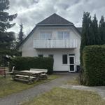 Ein zweistöckiges Haus mit Balkon, Garten und Holztisch. Umgeben von Bäumen und Hecken.