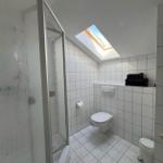 Badezimmer mit Dusche, Toilette und Dachfenster. Weiße Fliesen und Handtücher.