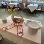 Tisch mit Tischdecke, Teller, Gabeln, Blumen und Eierkorb für Osterfest.