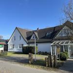 Weiße Ferienhaus mit Dachfenstern und Glasveranda. Grün bewachsenes Grundstück mit Holzpfosten.