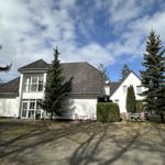 Wohnhaus mit Garten, Tischen und Stühlen unter Bäumen.