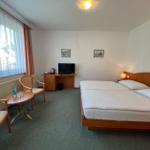 Zimmer mit Doppelbett, Schreibtisch, Fernseher und Sitzgelegenheit neben Fenster.