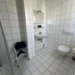 Badezimmer mit Dusche, Waschbecken, Toilette und Handtuchwagen.