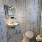 Badezimmer mit Waschbecken, Spiegel, Toilette und WC-Behälter.