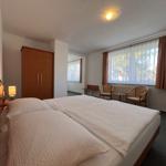 Schlafzimmer mit Doppelbett, Kleiderschrank, Sitzgelegenheit und Fenster mit Vorhängen.