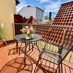 Terrasse mit Tisch, zwei Stühlen und Pflanze. Blick auf rote Dächer und Himmel.