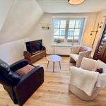 Wohnzimmer mit zwei Sesseln, Fernseher und Holzboden.
