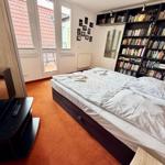 Schlafzimmer mit Bett, Bücherregal und Fenster zum Balkon.