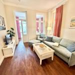Wohnzimmer mit Sofa, Couchtisch und Holzboden. Fenster mit roten Vorhängen.