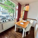 Esszimmer mit Holztisch, Stühlen und großem Fenster. Rote Vorhänge und Lampe.