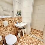 Badezimmer mit Toilette, Waschbecken und Dusche. Wand- und Bodenfliesen in warmen Tönen.