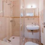 Badezimmer mit Dusche, Waschbecken und Toilette. Fliesenwand und Holzfußboden.