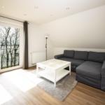 Wohnzimmer mit grauem Sofa, weißem Tisch und Balkontür zum See.