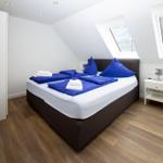 Schlafzimmer mit Dachschrägen, Bett mit blauer Bettwäsche und Holzboden.