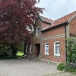 Rotes Ziegelhaus mit Eingang, Fenstern und Vorgarten mit Baum und Blumen.