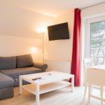 Wohnzimmer mit Sofa, Couchtisch und TV. Rote Vorhänge und Fenster mit Blick.