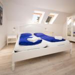 Schlafzimmer mit Doppelbett, blauer Bettwäsche, zwei Dachfenstern und weißem Schrank.