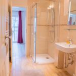 Badezimmer mit Dusche, Waschbecken und Toilette. Holzfußboden und Tür zum Balkon.