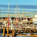 Harbor with boat masts, houses, and wind turbine under blue sky.