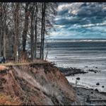 Path along a cliff with view of the sea and trees in the background.