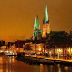Night view of Lübeck harbor with prominent church towers and illuminated buildings along the water.