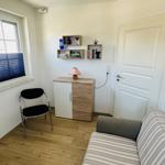Ein Raum mit Sofa, Stuhl, Schrank und Fenster mit Jalousie.
