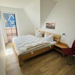 Schlafzimmer mit Doppelbett, Fenster und roter Sitzgelegenheit.