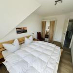 Schlafzimmer mit Doppelbett, Kleiderschrank und Wandbild unter Dachschräge.