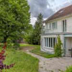 Haus mit Balkon, Grill und Gartenweg unter Bäumen.