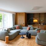 Wohnzimmer mit Sofa, Sessel und Holzmöbel. Große Fenster mit Blick auf Garten.