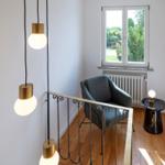 Lichtdurchfluteter Raum mit grauer Sitzgelegenheit und schmiedeeisernem Geländer.