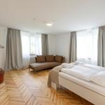 Schlafzimmer mit Bett, Sofa und Holzboden. Fenster mit Vorhängen.
