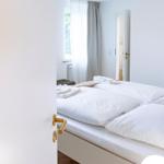 Schlafzimmer mit weißem Bett, Holzboden und Fenster mit Vorhängen.