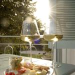 Zwei Weingläser und ein Teller mit Käse, Tomaten und Oliven auf einer Terrasse.