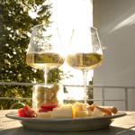 Zwei Weingläser und eine Platte mit Käse, Tomaten und Oliven auf einer Terrasse.