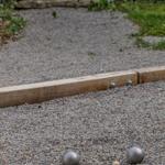Pétanque-Bälle liegen auf Kies im Garten. Hintergrund: Steinstufen und Vegetation.