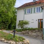 Ein zweistöckiges Haus mit weißer Fassade, grünen Fensterläden und einem Steinweg.