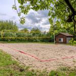 Sandplatz mit Volleyballnetz und kleinem Holzhaus im Hintergrund.