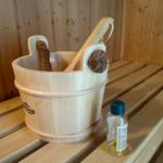 Holzbadewanne mit Besen und Flasche auf Sitzbank in Sauna.
