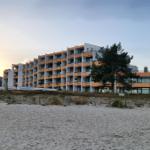 Strandvorsprung mit modernem Mehrfamilienhaus mit Balkonen und Sandstrand im Vordergrund.