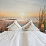 Schlafzimmer mit Bett, Kissen und Wandbild von Strand und Sonnenuntergang.