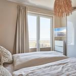 Schlafzimmer mit Blick auf Strand und Meer. Bett, Gardinen und Schrank sind sichtbar.