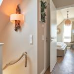 Haus mit Schlafzimmer und Dachschrägen. Holzgeländer und Wandlampe sichtbar.