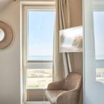 Ein Raum mit Fensterblick aufs Meer, Sessel und runder Wandspiegel.