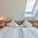Schlafzimmer mit Dachschräge, Doppelschreibtisch und Dachfenster.