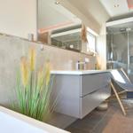 Badezimmer mit Waschtisch, Spiegel, Dusche und Liegestuhl