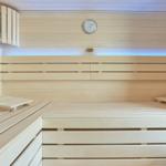 Holzsauna mit Sitzbänken, Thermometer und Eimer.